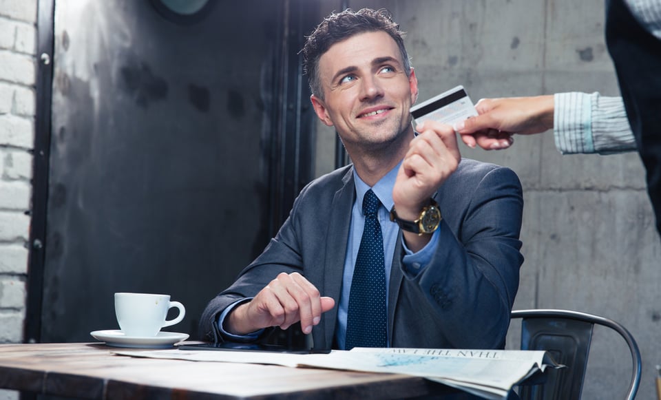 Happy businessman passing his credit card to waiter in cafe